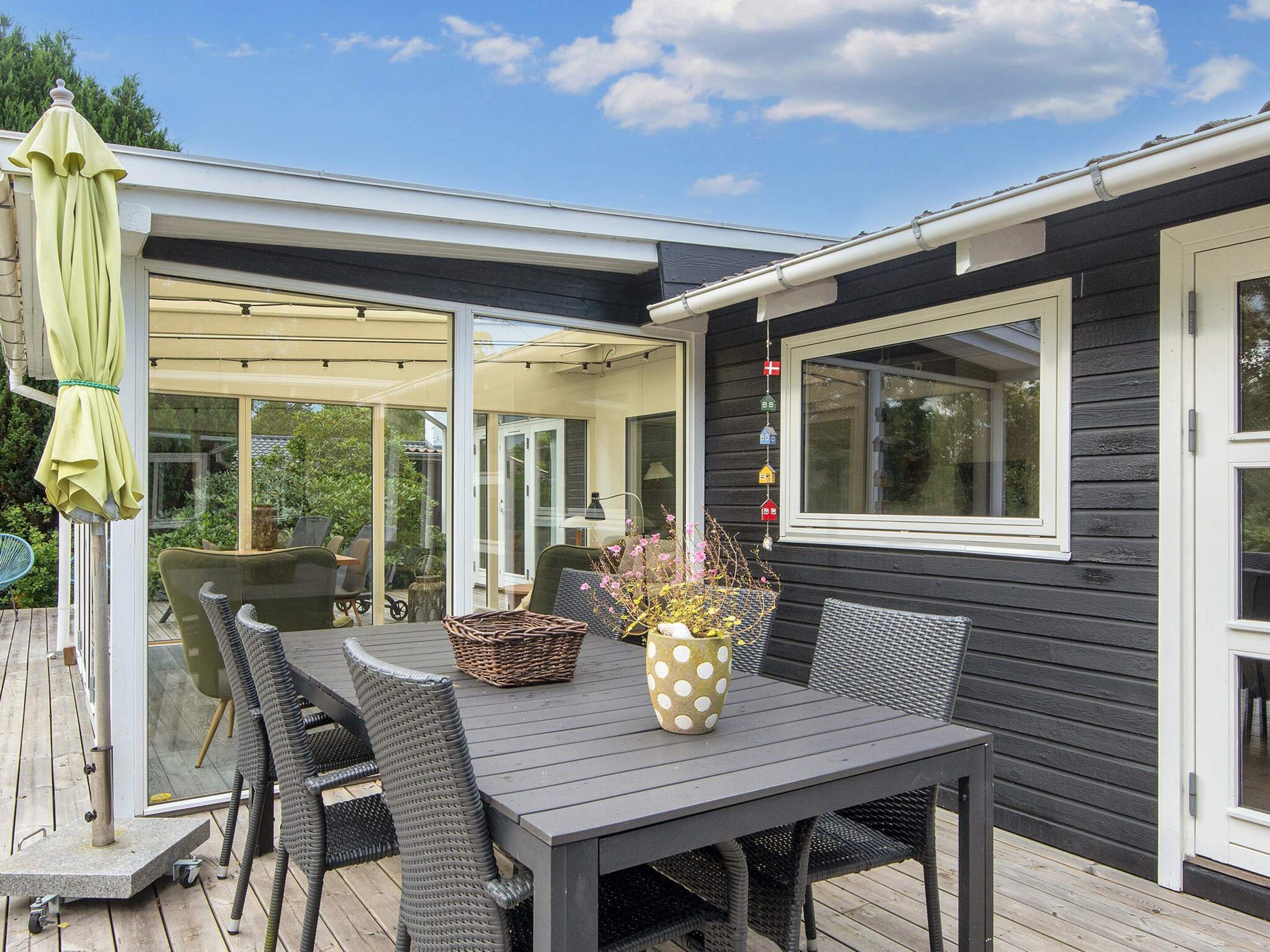 Une terrasse extérieure avec une table et des chaises, un espace salon abrité et une vue sur la verdure environnante.