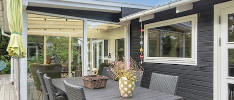 Un patio exterior con mesa y sillas, un área de estar techada y vistas a la vegetación circundante.
