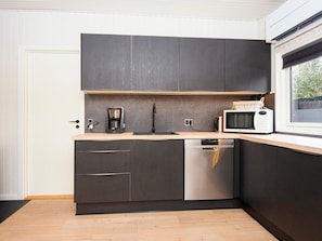 A modern kitchen with dark cabinetry, a built-in dishwasher, a coffee maker, and a microwave. - 4 Star Holiday Home in Grenaa (Grenaa)