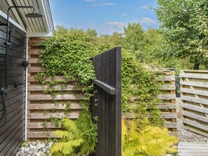 A wooden fence with climbing plants, a wooden bench, and a metal structure with a hose.