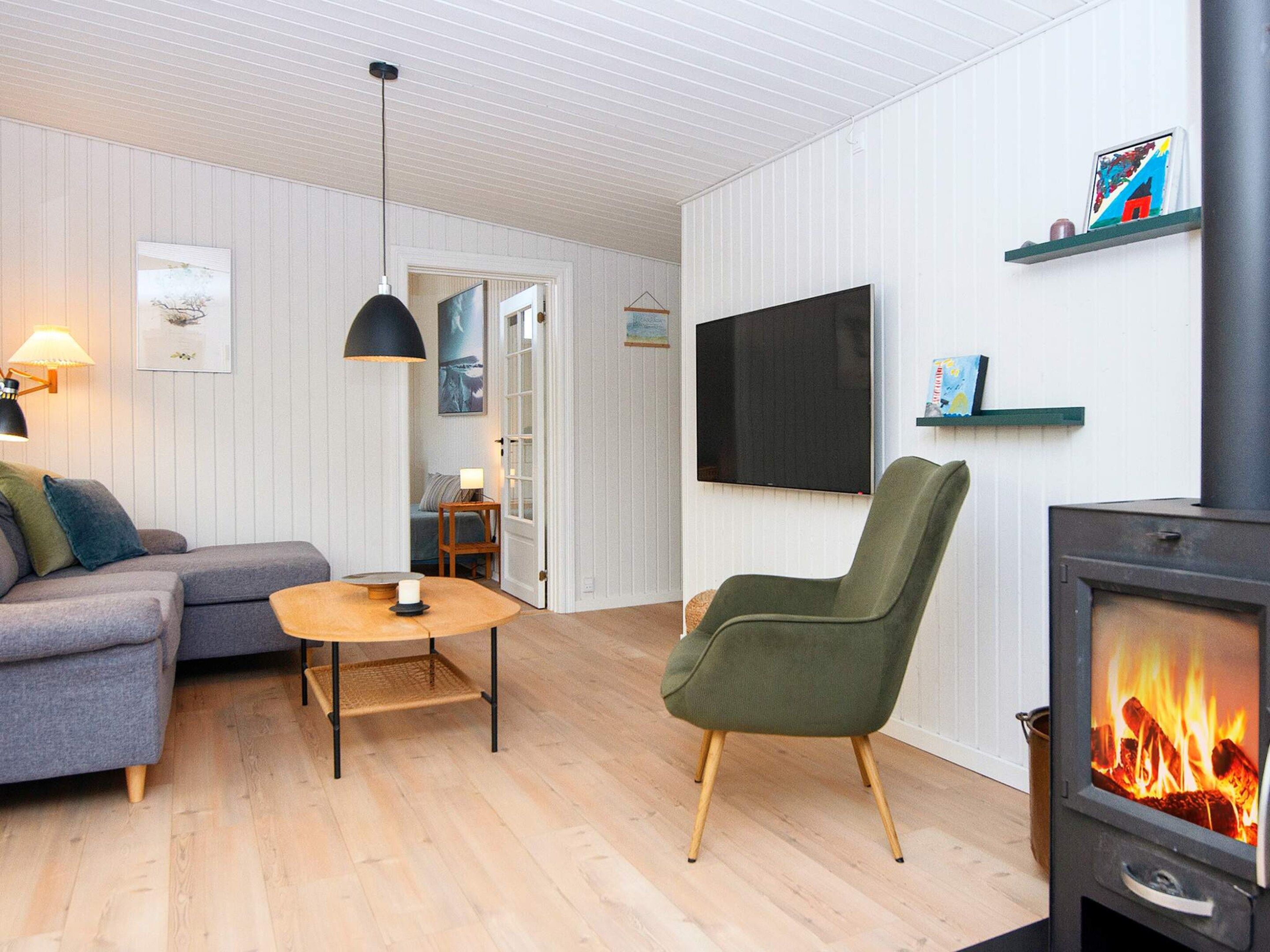 A living room with a sofa, a chair, a table, a TV, a fireplace, and a door leading to another room.