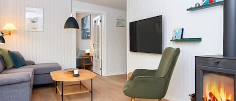 A living room with a sofa, a chair, a table, a TV, a fireplace, and a door leading to another room.