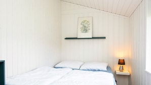 Quarto com cama, almofadas, mesa de cabeceira com abajur e quadro na parede.