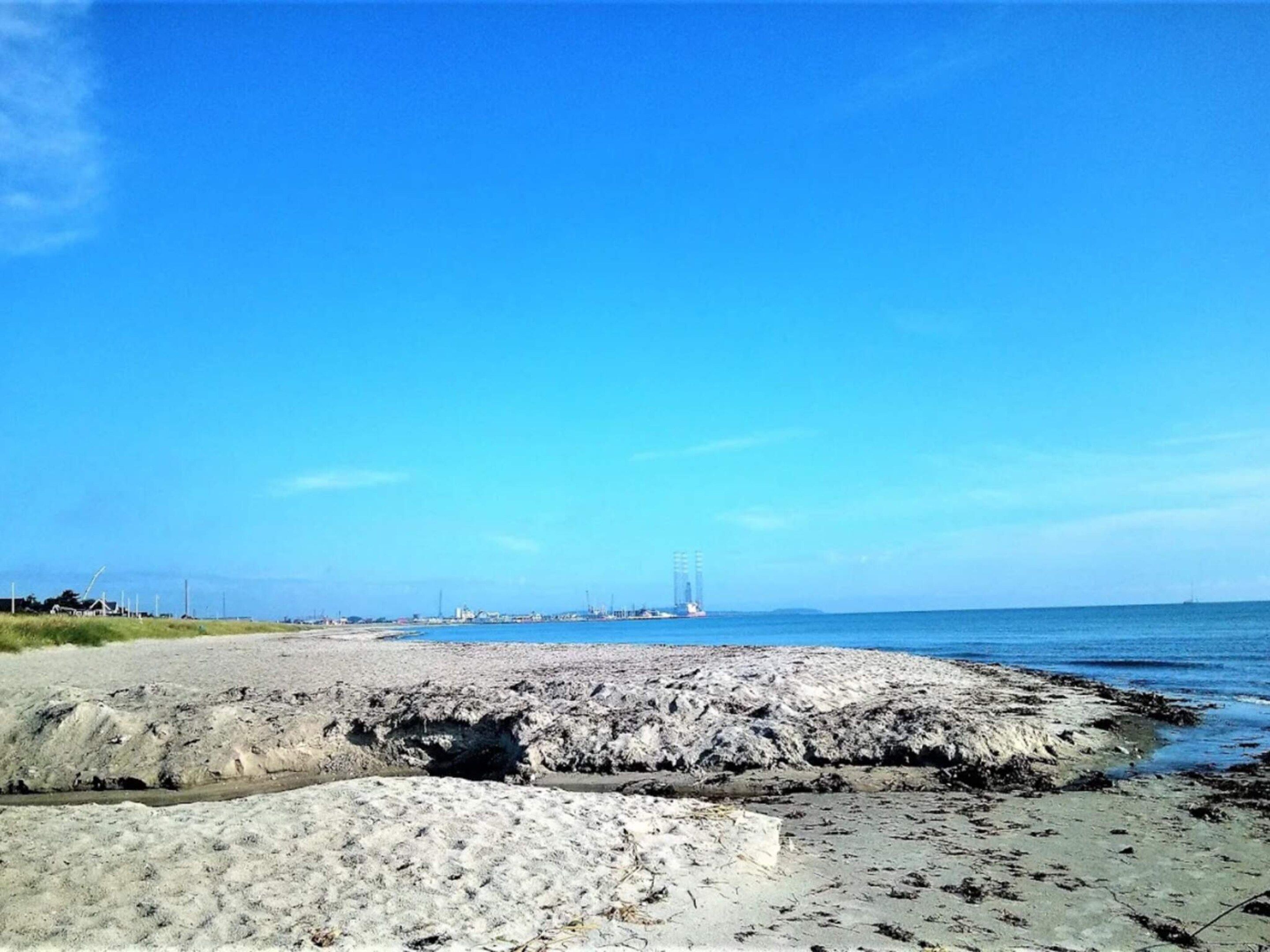 A beach with rocky terrain, a clear sky, and distant structures.