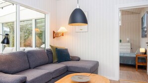 Uma sala de estar moderna com um sofá cinza, uma mesa de centro de madeira e uma luminária pendente preta.