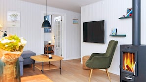 Uma sala de estar moderna com um sofá, uma mesa redonda de madeira, uma poltrona verde, uma TV e uma lareira a lenha.
