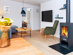 Un salon moderne comprenant un canapé, une table ronde en bois, un fauteuil vert, un téléviseur et un poêle à bois.