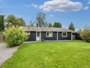 A single-story building with a dark exterior, a tiled roof, and a small front yard with a lawn and a gravel path.
