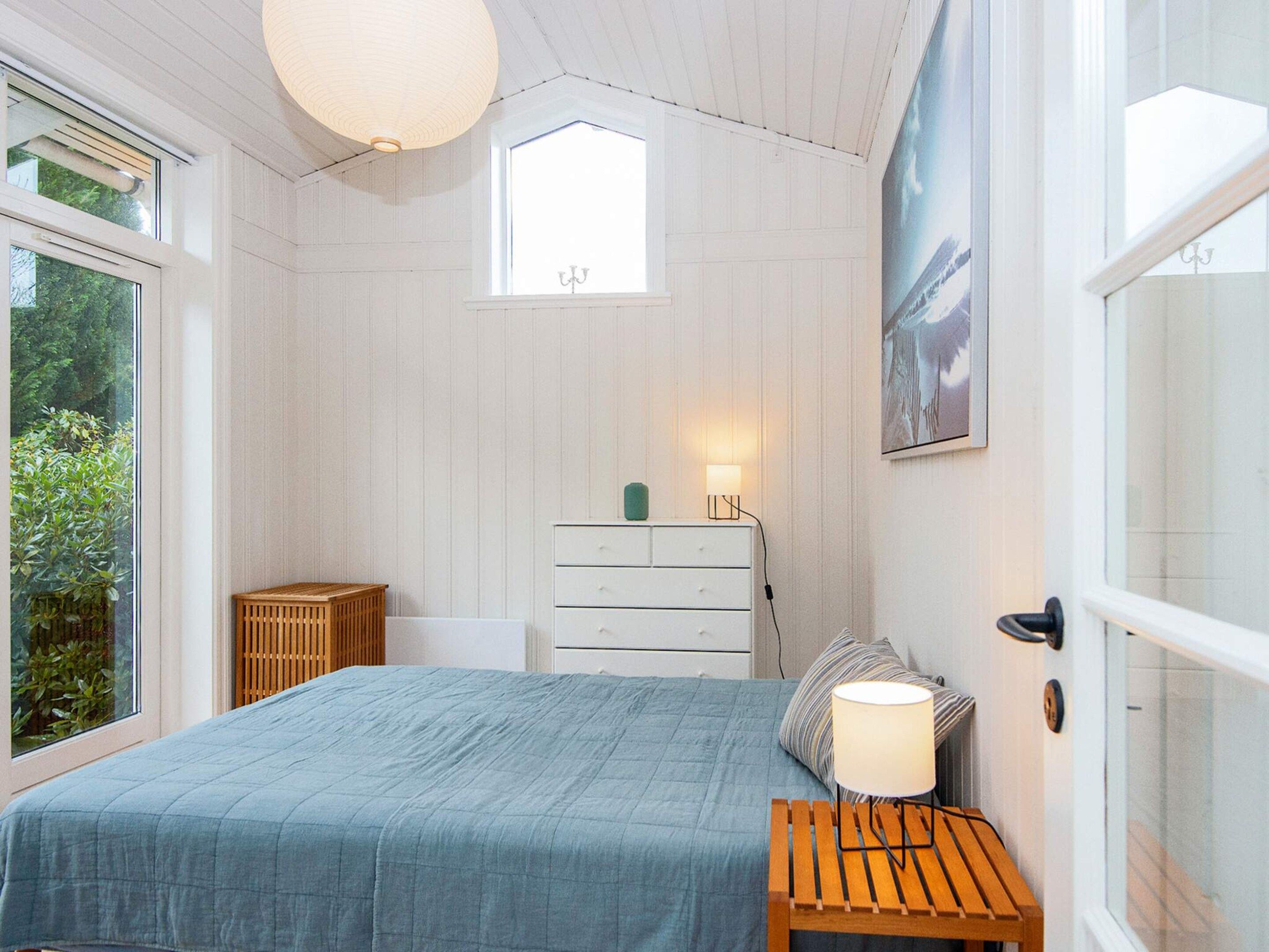 Et soveværelse med seng, kommode, sengebord, vindue og dør.