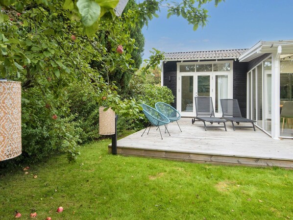 A patio with two chairs and a table, a covered area with a patterned lamp, and a house with a dark facade and glass doors.