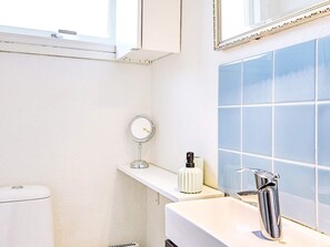 A modern bathroom with a white sink, chrome faucet, and a round mirror on a white shelf.