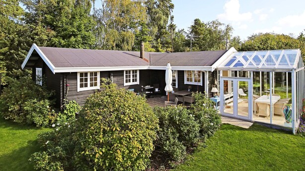 Une maison dotée d’une grande serre en verre, d’un patio couvert et d’une pelouse bien entretenue.
