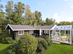 Ett hus med ett stort växthus av glas, en täckt uteplats och en välskött gräsmatta.