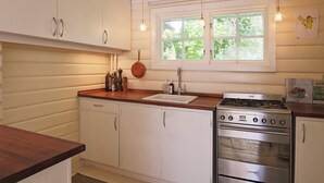 Une cuisine avec des meubles blancs, un plan de travail en bois, une cuisinière et une fenêtre donnant sur un espace verdoyant.
