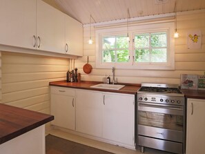 Une cuisine avec des meubles blancs, un plan de travail en bois, une cuisinière et une fenêtre donnant sur un espace verdoyant.