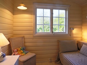 A cozy room with a window, a wicker chair, a small table with a lamp, and a striped sofa.