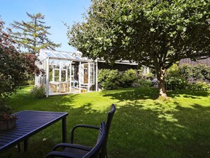 A conservatory with a glass roof, surrounded by a well-maintained lawn and a large tree.
