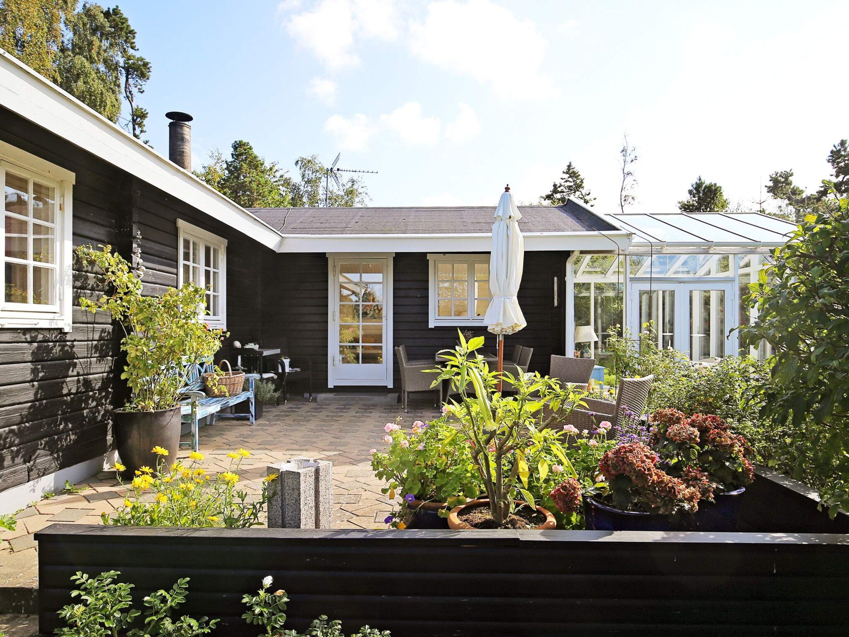 Ein Holzhaus mit Terrasse, Wintergarten und verschiedenen Blumentöpfen.