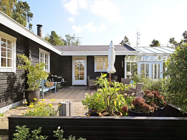 A wooden house with a patio, a conservatory, and various potted plants.