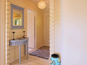 Un pasillo con piso de madera, una puerta blanca, un jarrón azul y un tapete estampado.