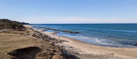 A coastal landscape with a pebbly beach, a rocky breakwater, and a clear sky.