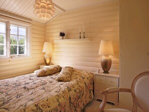 Un dormitorio con una cama, dos lámparas de noche, una mesita de noche, un aparador y una silla.