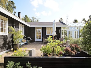 A wooden house with a conservatory, outdoor seating, and a garden.