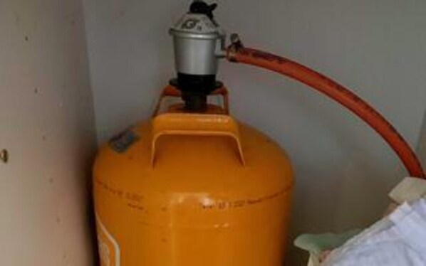 A large orange gas cylinder with a red hose attached, positioned against a wall.