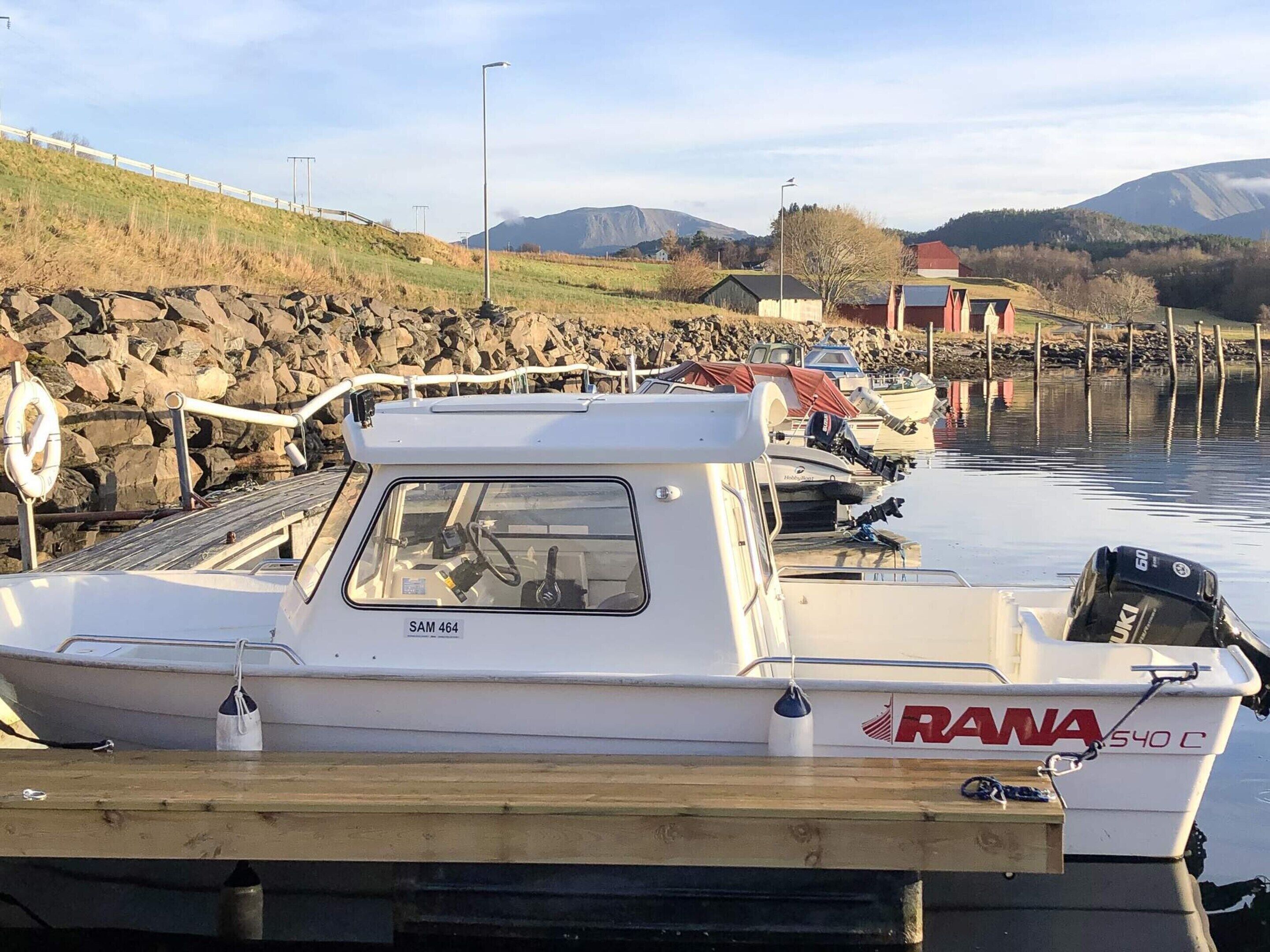 A marina with boats docked, a rocky shoreline, and a mountainous backdrop.