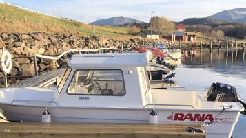 A marina with boats docked, a rocky shoreline, and a mountainous backdrop.