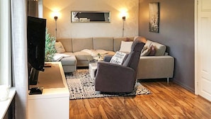 Een moderne woonkamer met een bank, fauteuil en een flatscreen televisie.