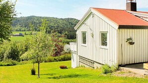 Een wit gebouw met een rood dak, omringd door groene velden en bomen, met een uitzicht op heuvels in de verte.