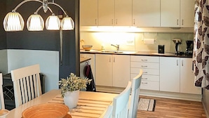 Een moderne keuken met witte kastjes, een geruit tafelkleed en een houten eettafel.