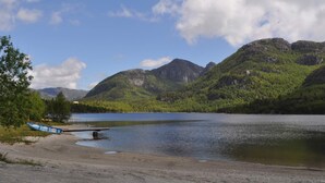 A lakeside view with mountains in the background, a dock, and a boat. - 4 Star Holiday Home in Jorpeland (Strand)