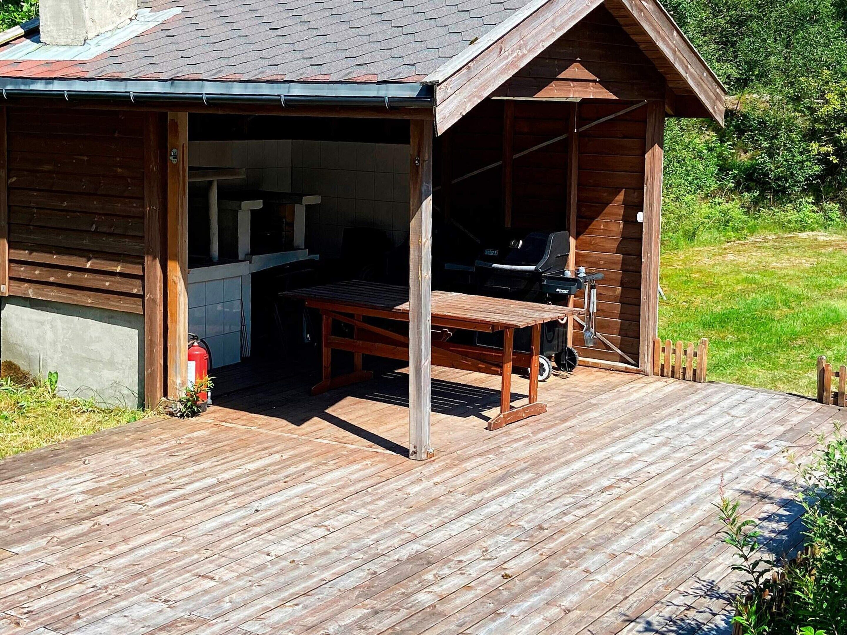 En træhytte med åben terrasse, grill og bord.