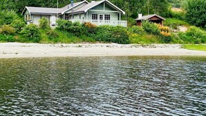 A lakeside cabin with a dock, surrounded by lush greenery and rocky hills. - 4 Star Holiday Home in Jorpeland (Strand)