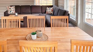 A dining area with a wooden table and chairs, a sofa with floral cushions, and a view through large windows. - 4 Star Holiday Home in Jorpeland (Strand)
