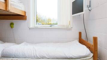 A single bed with a wooden headboard in a room with white walls and a window.