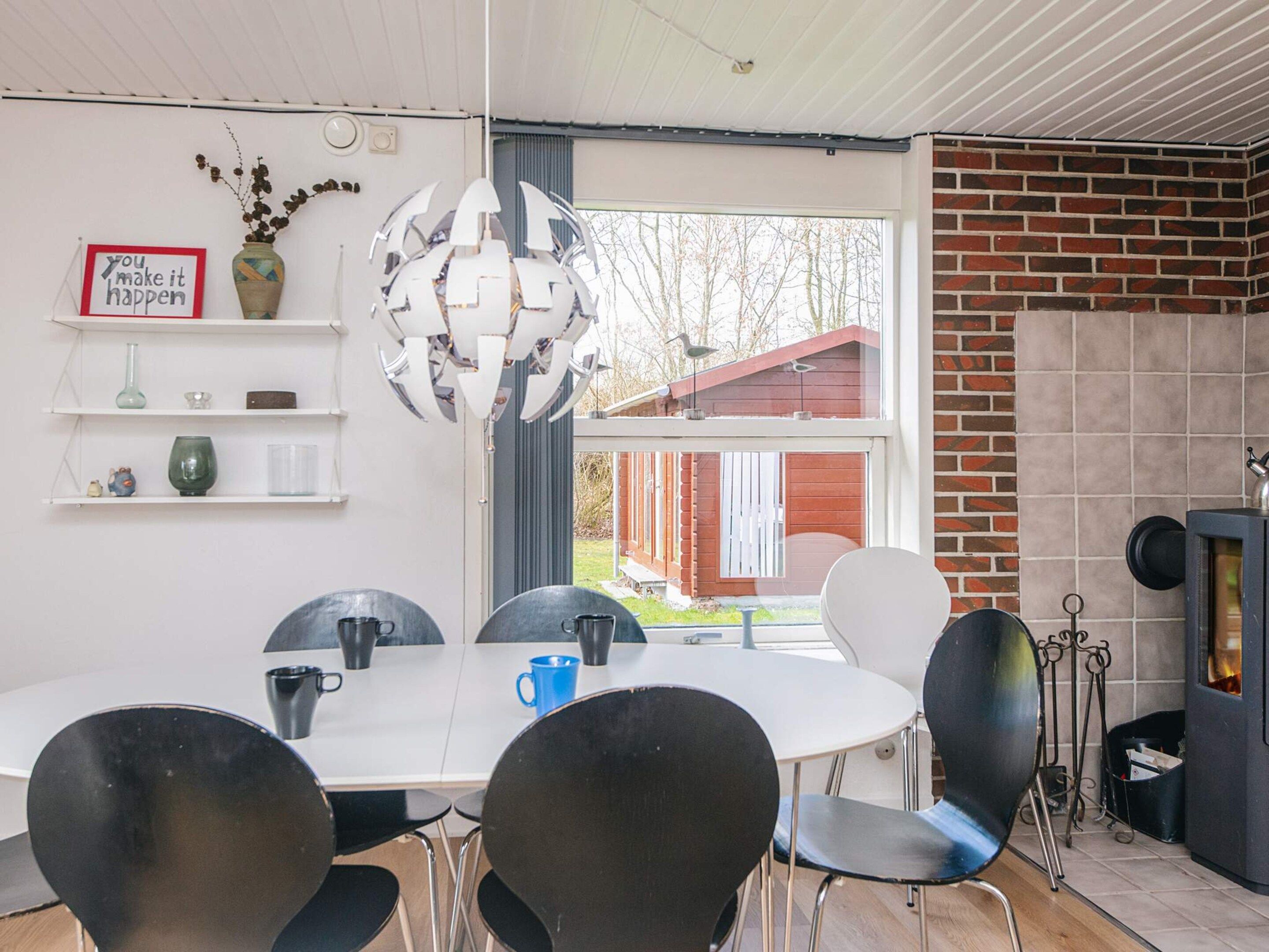A modern dining area with a white table, black chairs, a decorative metal chandelier, and a brick fireplace.