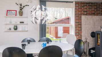 A modern dining area with a white table, black chairs, a decorative metal chandelier, and a brick fireplace.