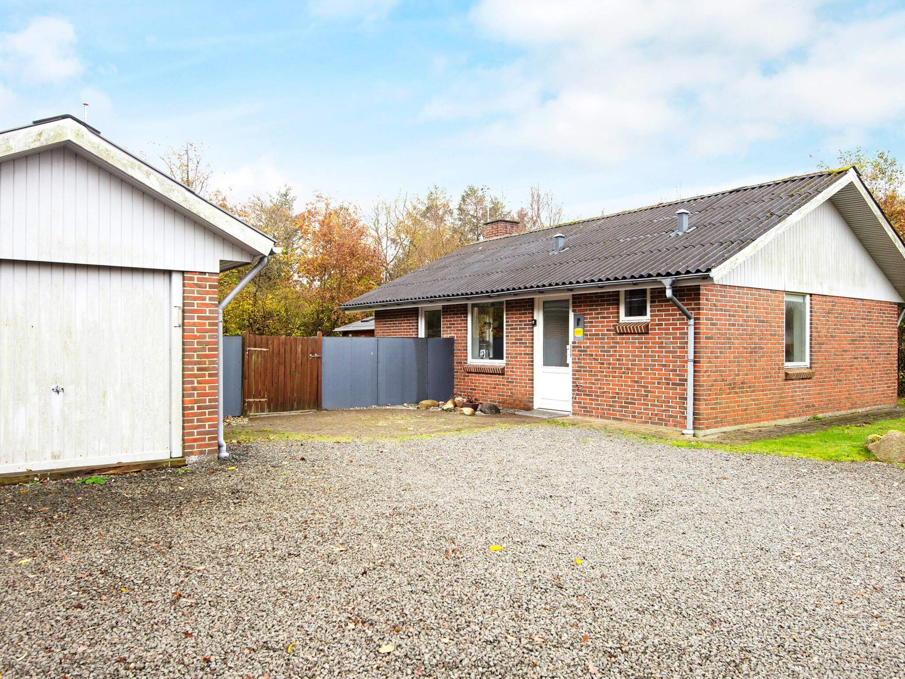 A single-story brick house with a gravel driveway, a wooden fence, and a detached garage.