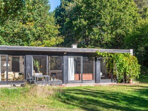 A modern house with large glass windows, a patio with outdoor furniture, and a garden area.