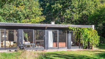 A modern house with large glass windows, a patio with outdoor furniture, and a garden area.