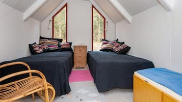 A small, cozy room with two beds, a wooden dresser, a chair, and a large window.
