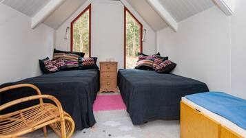 Una habitación pequeña y acogedora con dos camas, un aparador de madera, una silla y un ventanal grande.