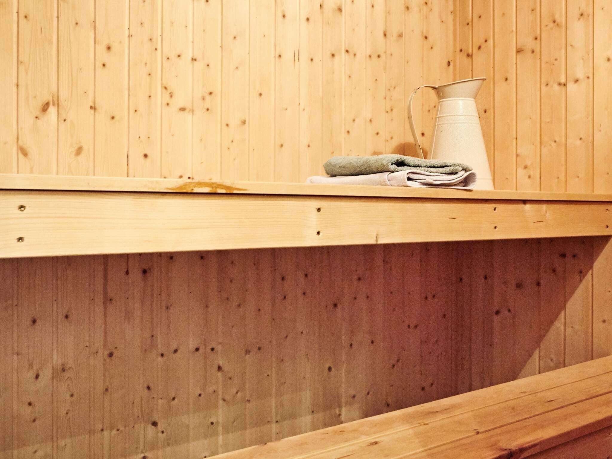 A wooden sauna bench with a towel and a white container on top.
