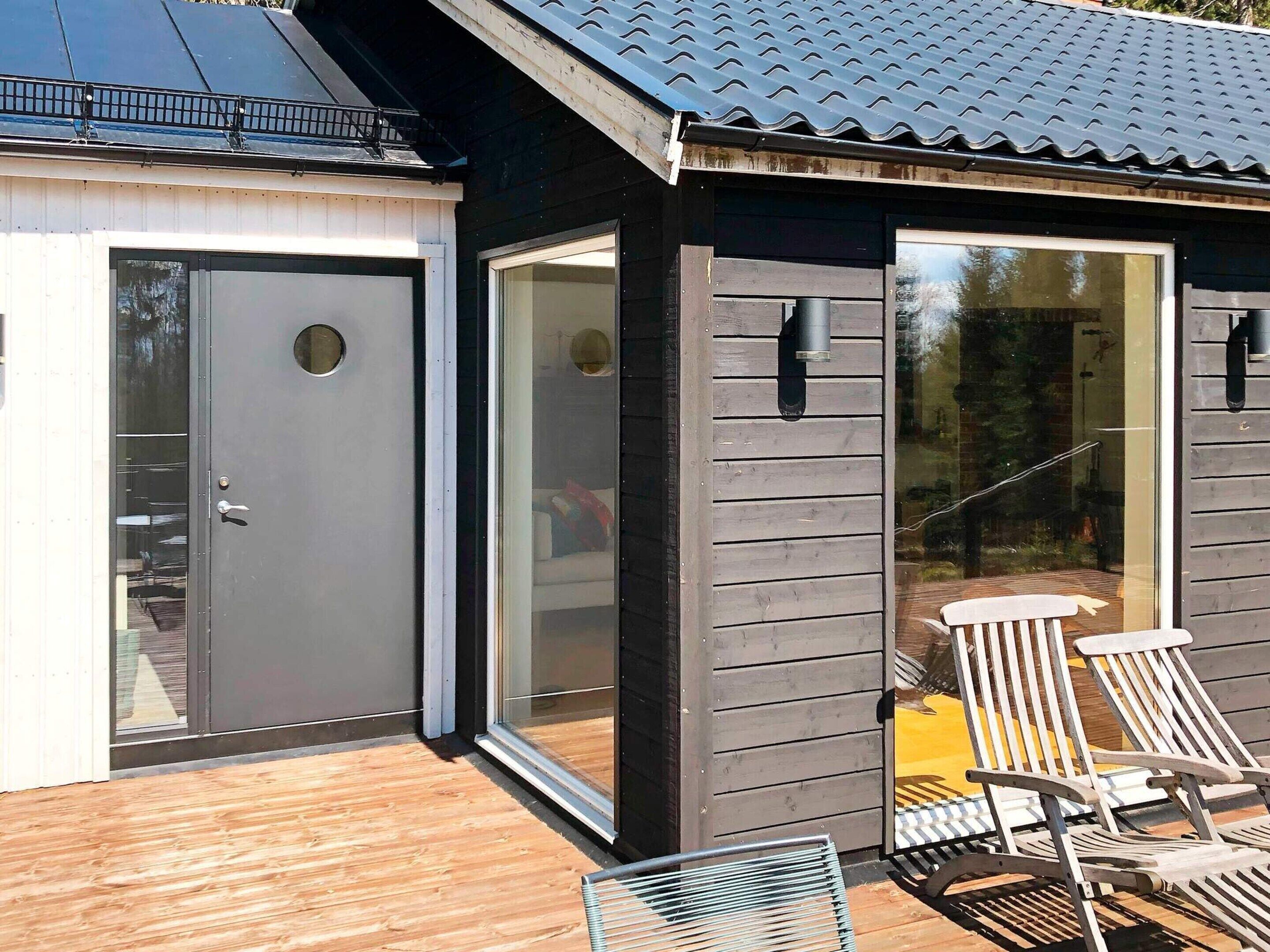 A modern building with a dark exterior, large sliding glass doors, and a wooden deck with two metal chairs.