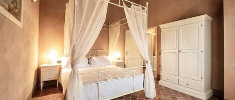 A bedroom with a four-poster bed, a nightstand, a cabinet, and a tiled floor.
