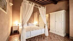 Een slaapkamer met een hemelbed, nachtkastje, kast en betegelde vloer.