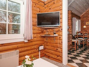A cozy cabin interior with a mounted flat-screen TV, wooden walls, a dining area with a checkered floor, and a radiator. - 6 Person Holiday Home in Hovborg (Hovborg)